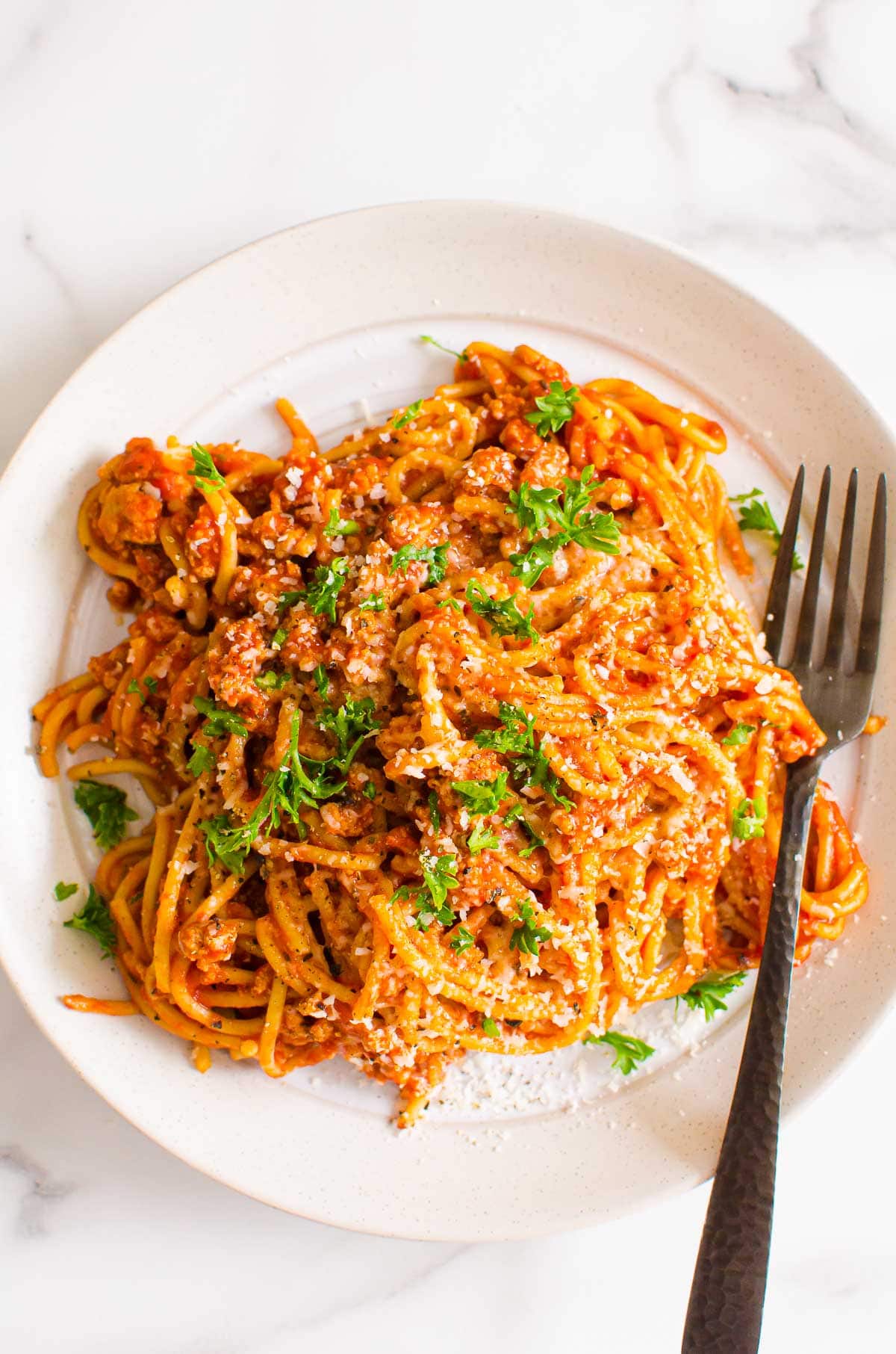 Instant pot spaghetti on plate with fork and garnished with parsley.