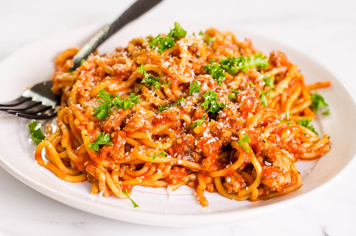 Instant pot spaghetti on white plate garnished with parsley and parmesan cheese.