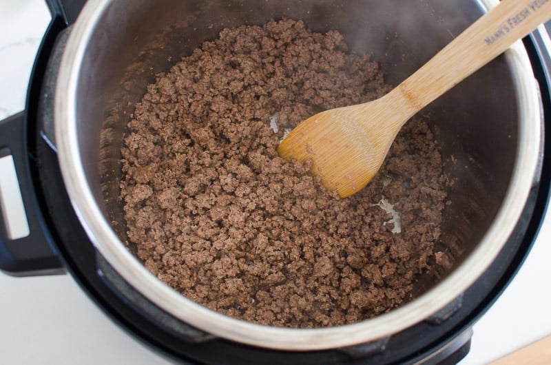 Browned ground beef and wooden spatula in Instant Pot.