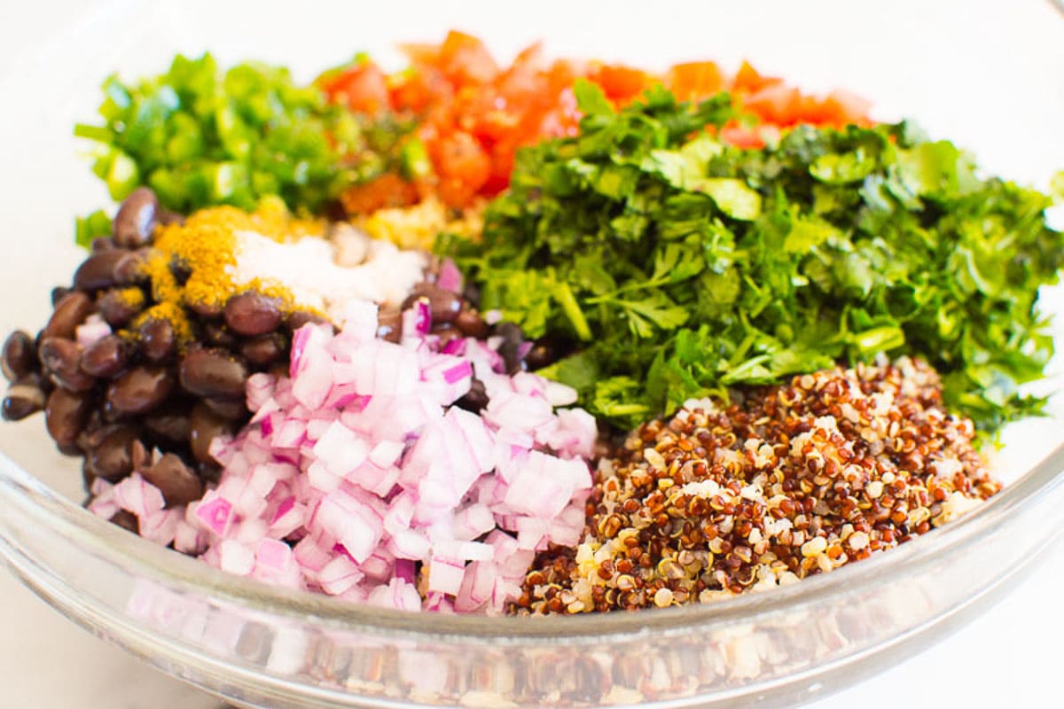 Chopped onion, cilantro, tomatoes, jalapeno with black beans, quinoa and spices in bowl.