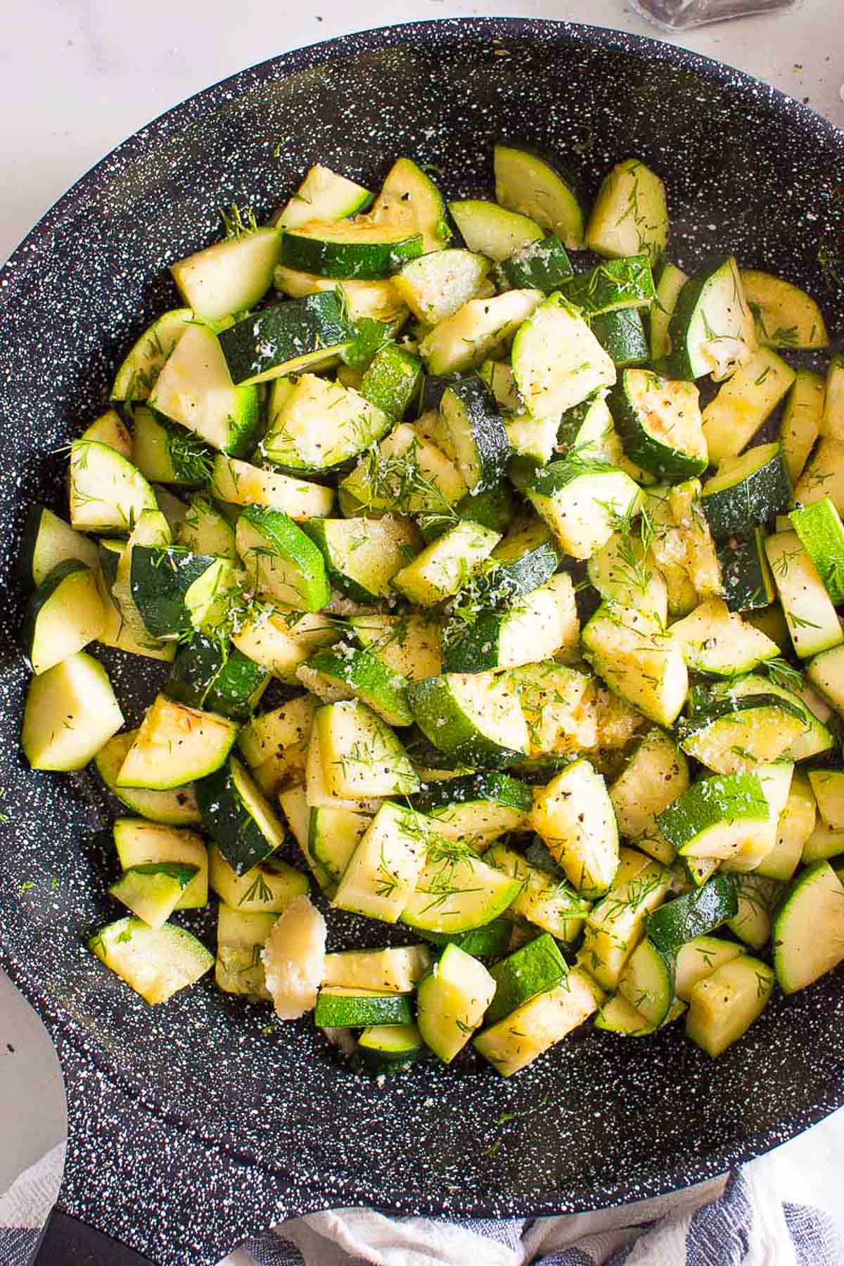 Sauteed zucchini in a skillet garnished with dill and Parmesan.