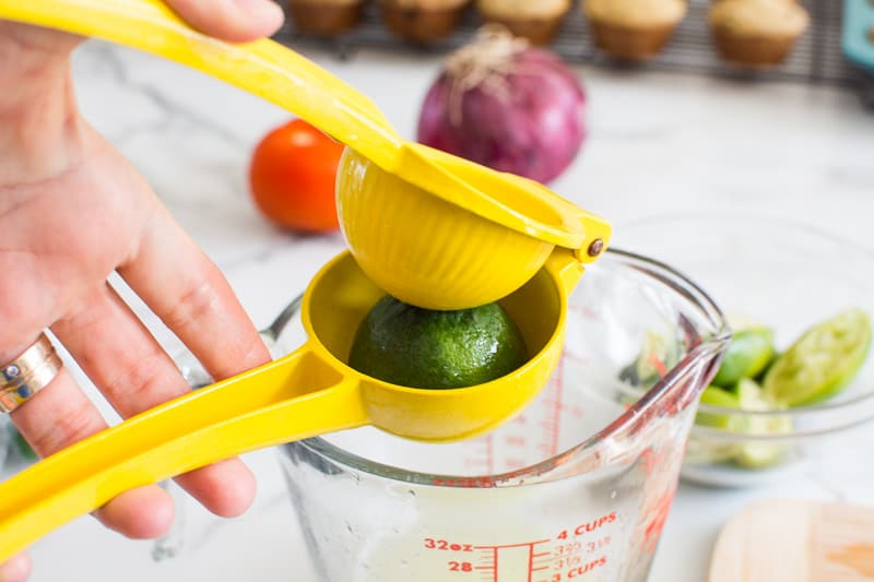 Squeezing juice from lime with a lime squeezer over a bowl.