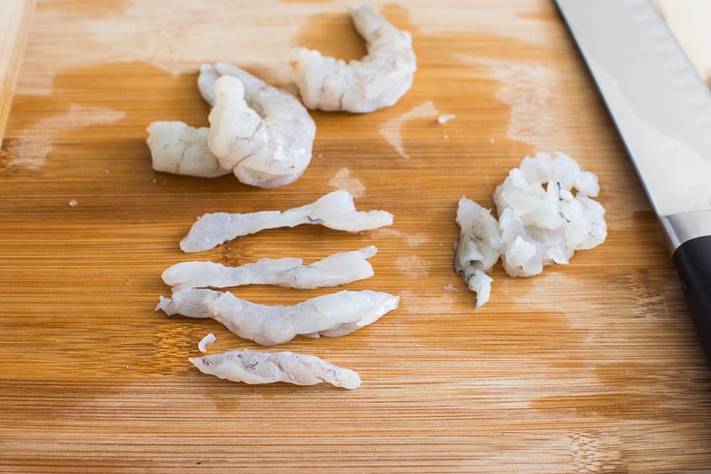 Deveined and chopped shrimp on cutting board with a knife.