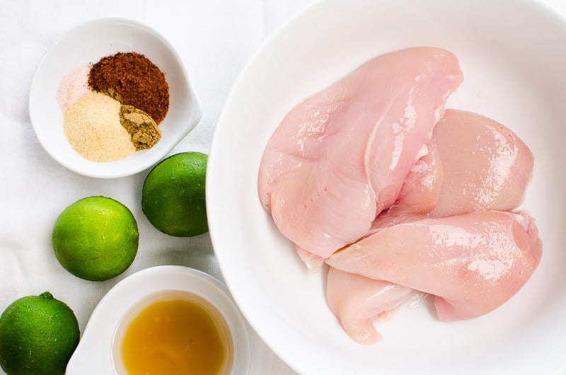 Chicken breasts, spices, maple syrup in separate bowls and three limes.