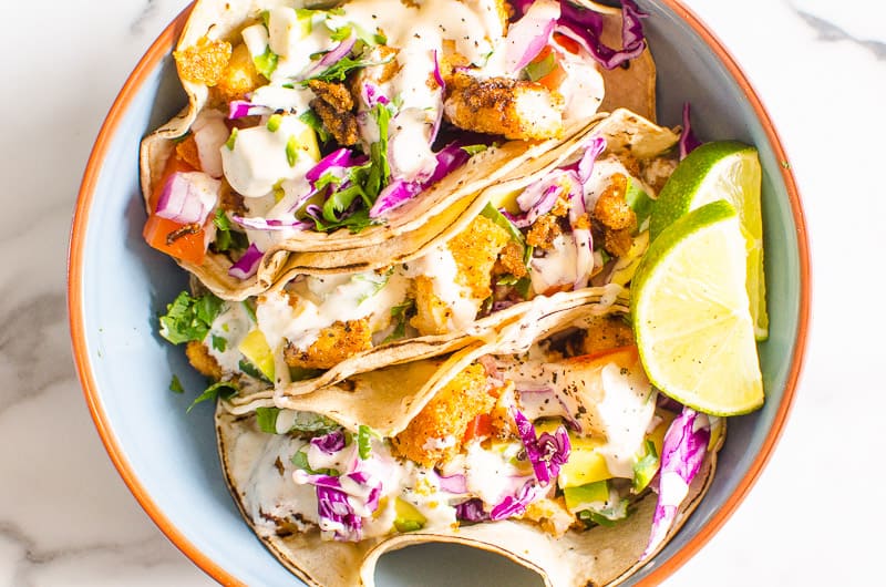 fish taco recipe served with crema, fixings and lime in a blue bowl