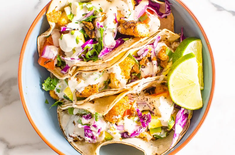 fish tacos in a bowl with lime and red slaw