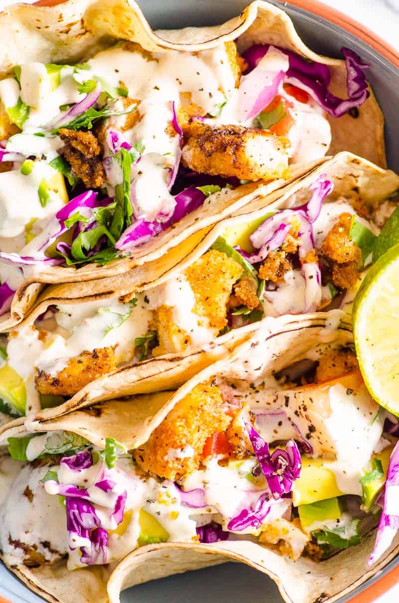Three fish tacos with slaw and fish taco sauce in blue bowl. 