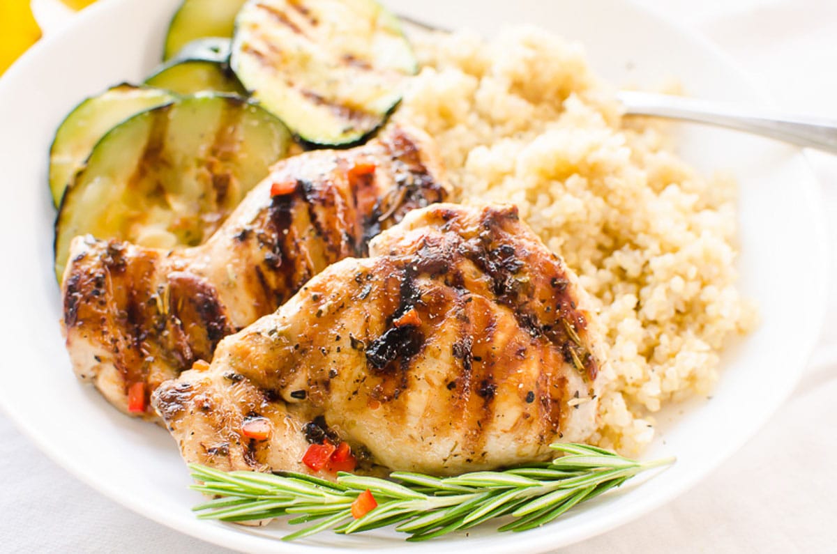 Greek chicken on a plate with quinoa, grilled zucchini and rosemary.