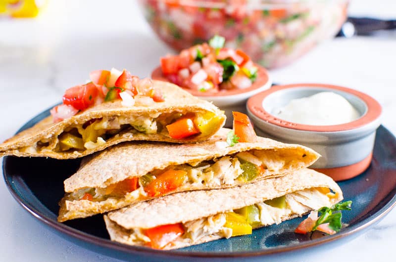 Quesadillas stacked on a plate with bowls of salsa and sour cream. 