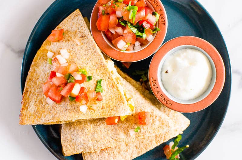 Looking down at 3 wedges of quesadilla pieces on a blue plate with salsa and sour cream. 
