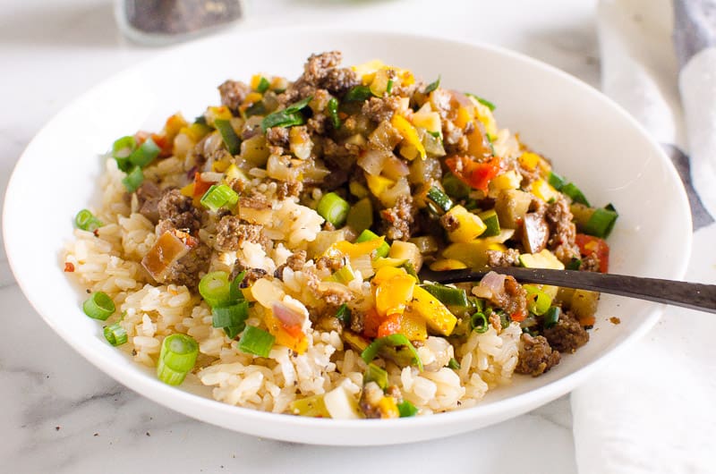 Ground beef with veggies and rice served in white bowl with a fork.