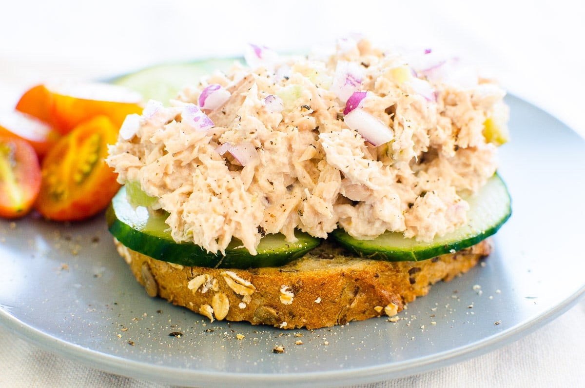 Healthy tuna salad served on toast with cucumbers on blue plate with tomatoes.