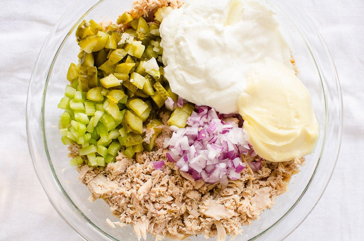 Chopped pickles, red onion, celery, flaked tuna, yogurt and mayo in a bowl.