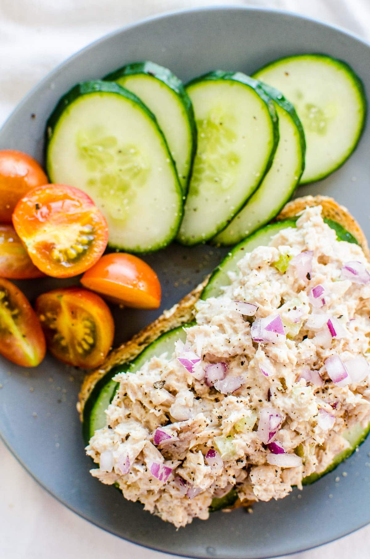 Healthy tuna salad on a toast garnished with red onion on blue plate with tomatoes and cucumbers.