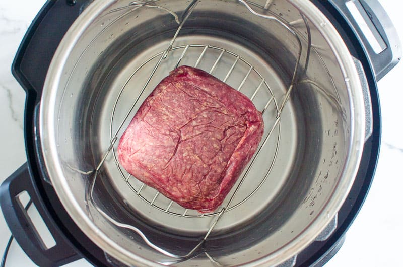 Water, trivet and frozen ground beef pack on top in Instant Pot.
