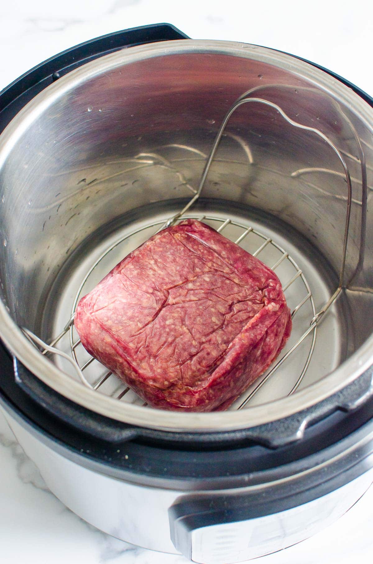 Instant Pot frozen ground beef on trivet in Instant Pot.