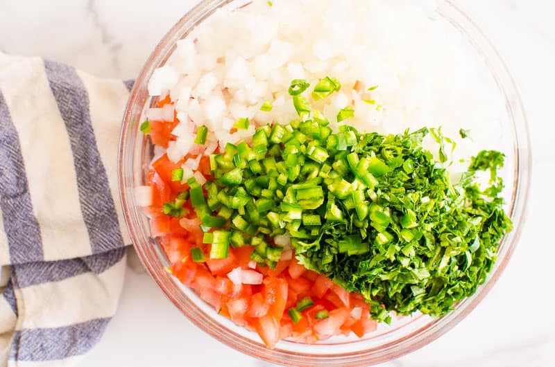 tomato, onion, cilantro, jalapeno chopped in a bowl and towel nearby