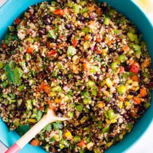 Southwest quinoa salad in blue bowl with wooden spoon.