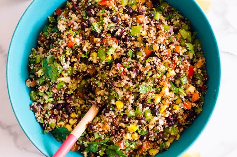 southwest quinoa salad in a blue bowl with a serving spoon