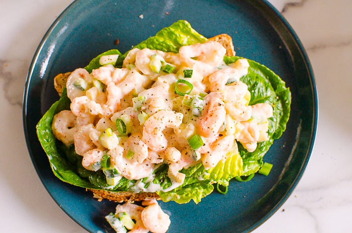 Healthy shrimp salad plated with lettuce and slice of bread.