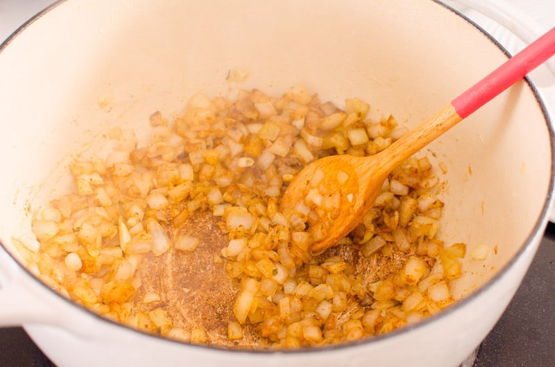 Sauteed onion with spices in a pot with spoon.
