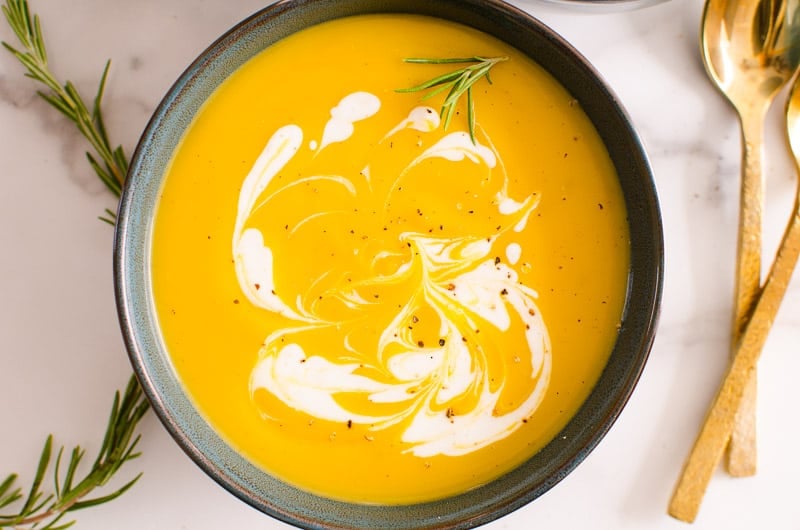 Bowl of instant pot butternut squash soup garnished with rosemary and cream.