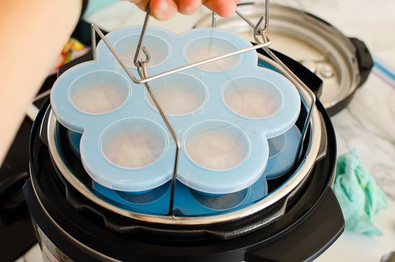 Egg bite molds with lids on a trivet being lowered into Instant Pot.