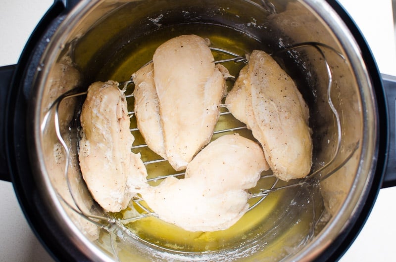 Four cooked Instant Pot frozen chicken breasts on a trivet inside the pot.