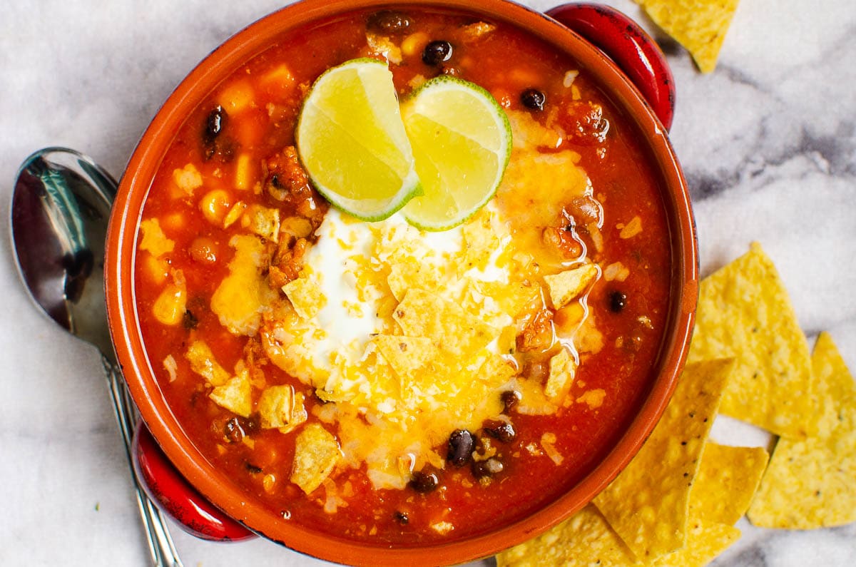 Bowl of instant pot taco soup garnished with cheese, tortilla chips and lime.