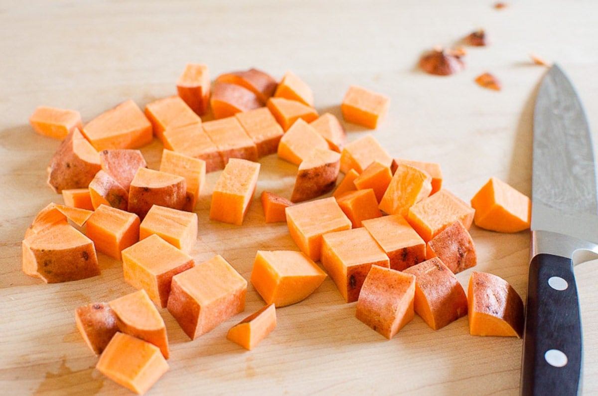 Yam cut into cubes on a cutting board with knife.