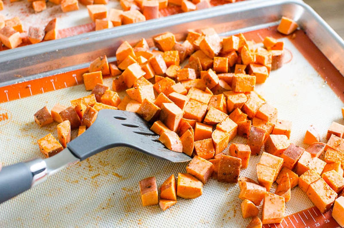 Cubed sweet potatoes on baking sheet with seasonings and oil.