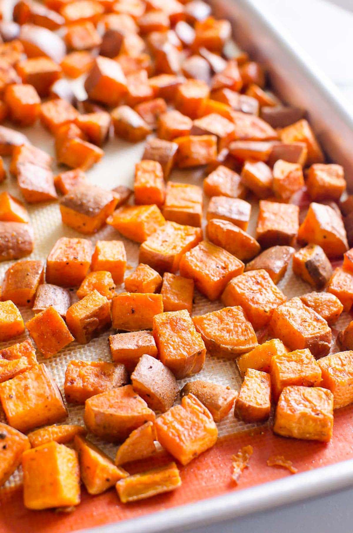 Healthy oven roasted sweet potatoes on silicone lined baking sheet.