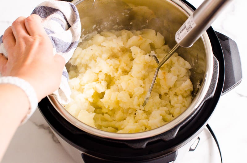 Mashing instant pot mashed potatoes with a masher inside the pot. 