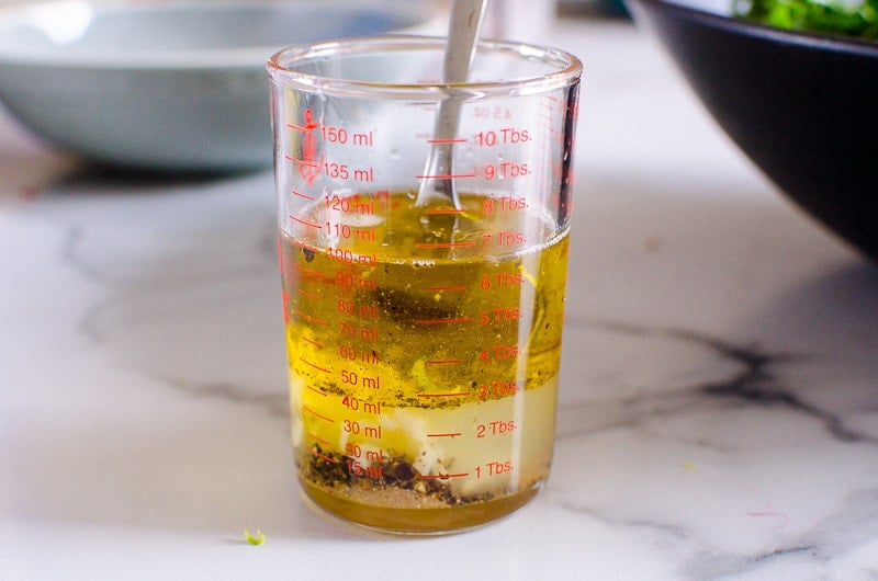 Olive oil, garlic and seasonings whisked with a fork in glass cup. 