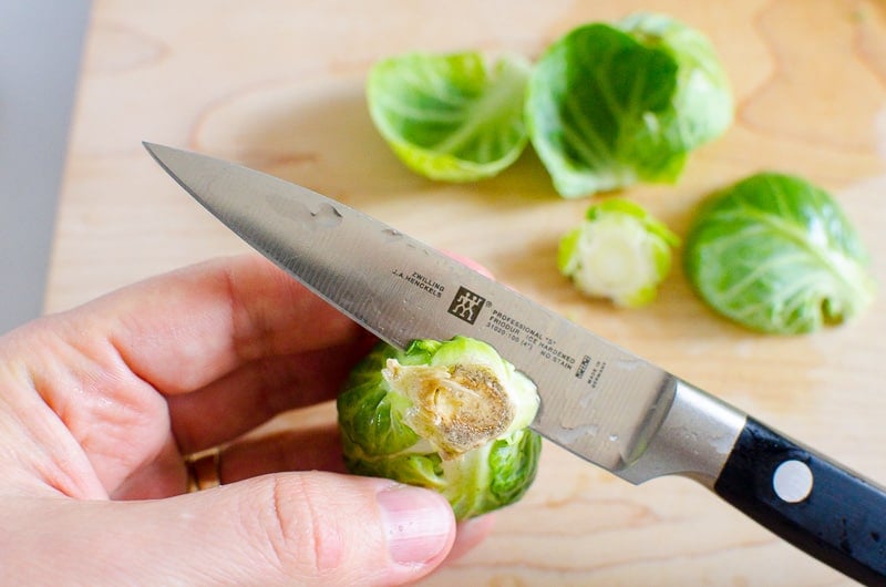 Hand holding a Brussels sprout and showing how to trim the end with paring knife. 