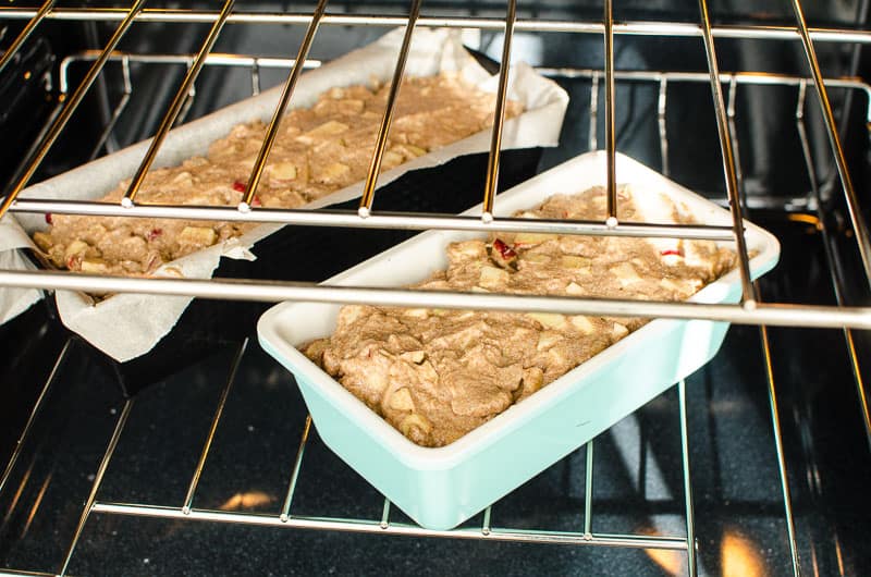Two loaf pans of bread with apples in the oven.
