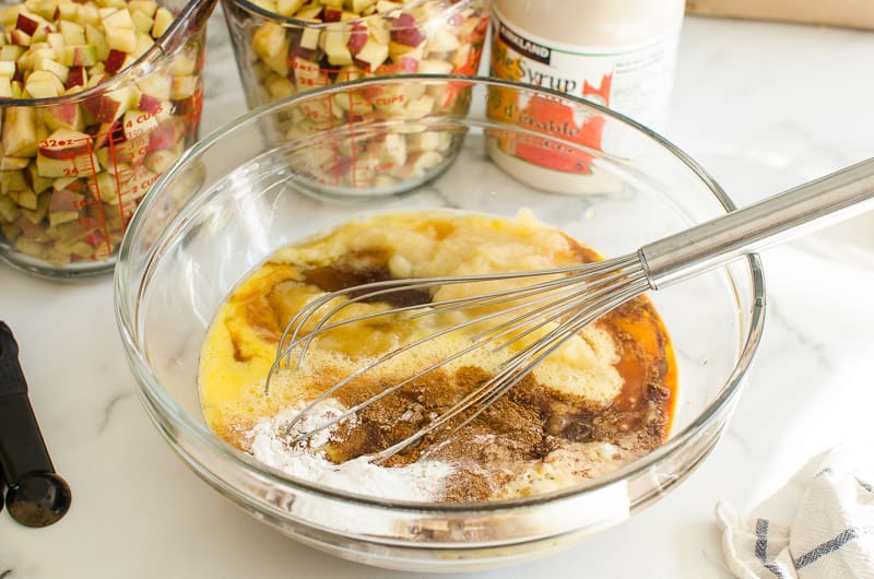 Whisking egg, maple syrup, applesauce, cinnamon and baking staples in bowl.