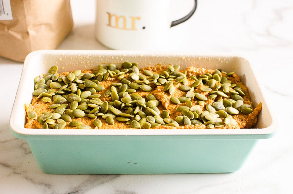 unbaked pumpkin bread sprinkled with pumpkin seeds in loaf pan