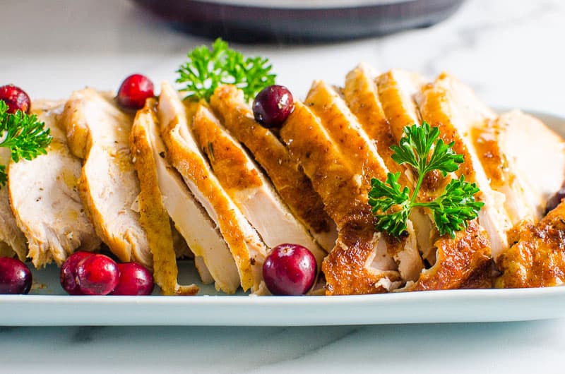 sliced Instant Pot Turkey Breast on a platter garnished with cranberries and parsley