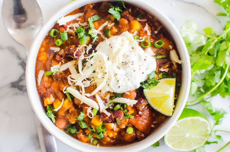 A bowl of chili with lime wedge, cheese and sour cream. 