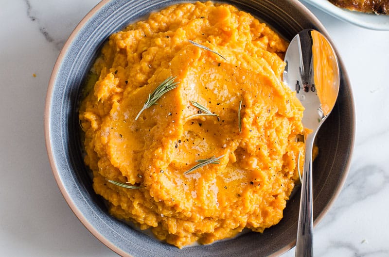 bowl of mashed sweet potatoes with a garnish of rosemary