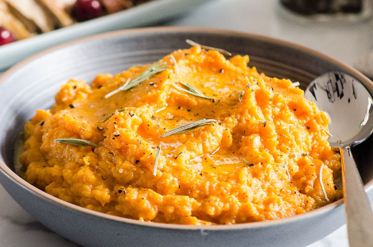 Mashed sweet potatoes in a blue bowl with a spoon.