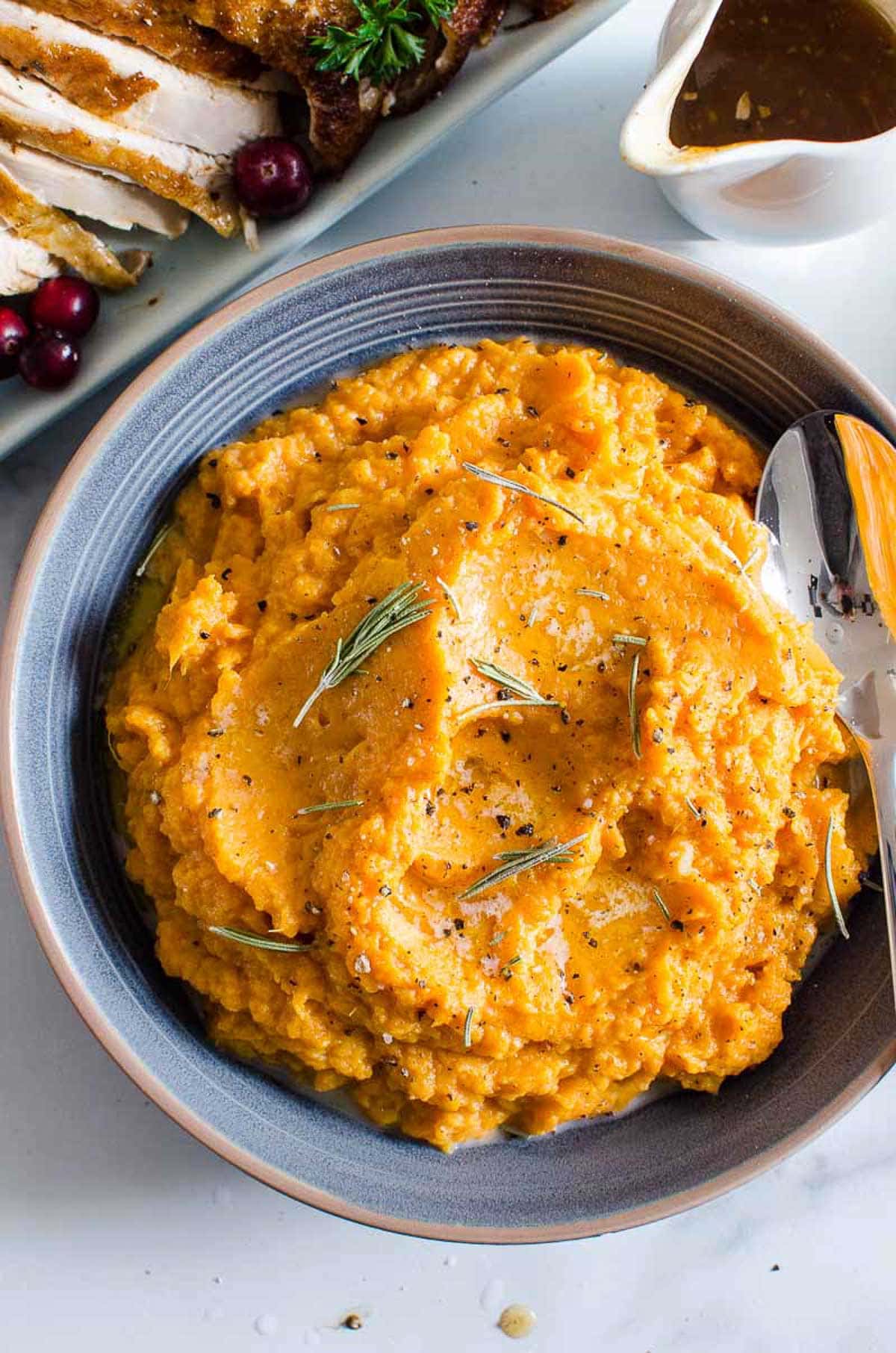 Healthy mashed sweet potatoes in a bowl with a spoon and fresh rosemary garnish.