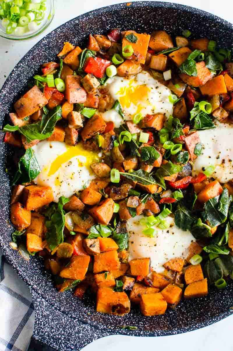 Sweet potato hash in skillet with eggs and green onion. 