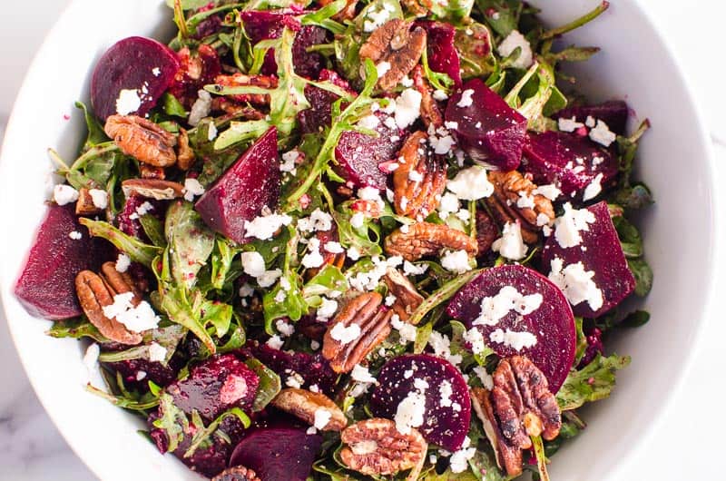 Beet salad with arugula, feta and pecans in a large white salad bowl