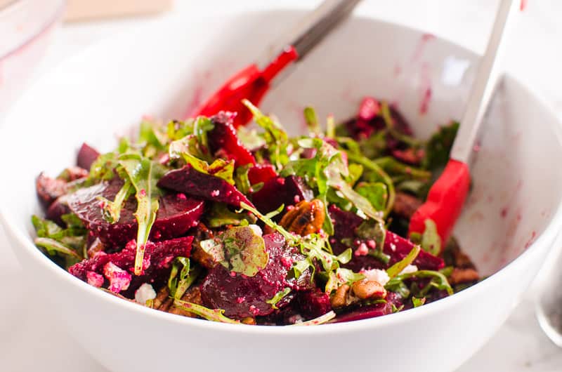 Arugula beet salad in white bowl with tongs.