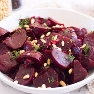 Instant Pot beets in a white bowl with dill and pine nuts.