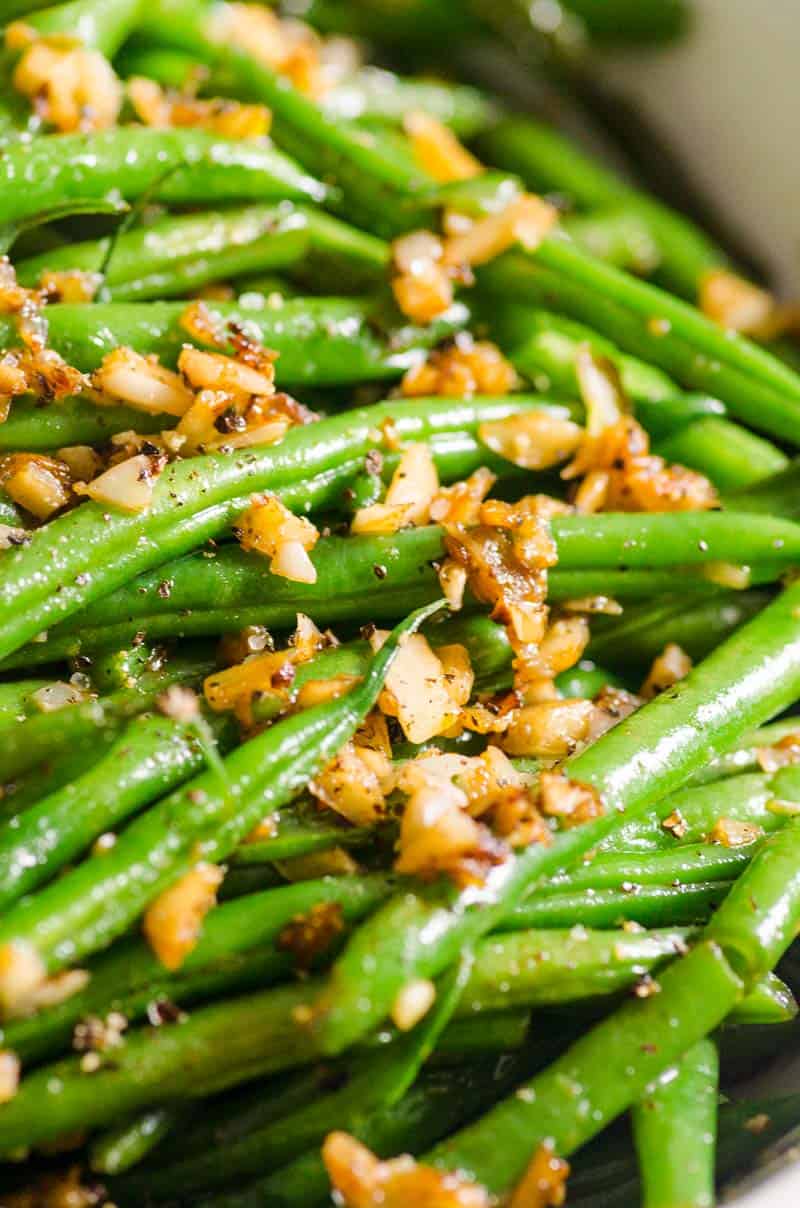 Closeup of cooked green beans topped with garlic slivers.