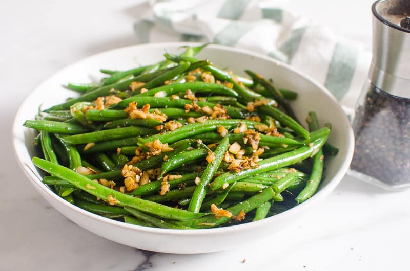 Garlic Green Beans in a white bowl with towel and pepper jar on a table