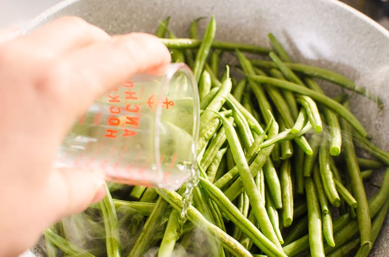 adding water to fresh green beans in skillet